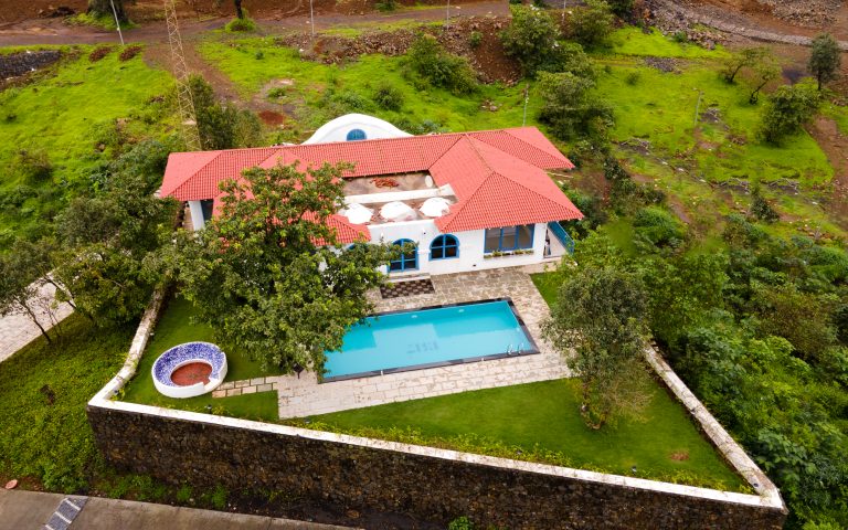 A beautiful Greek home with white walls, red roof tiles, and blue shutters, surrounded by olive trees and overlooking the blue sea.