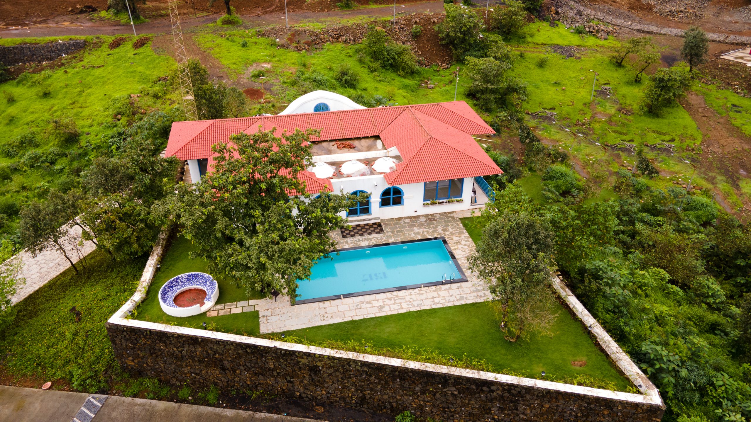 A beautiful Greek home with white walls, red roof tiles, and blue shutters, surrounded by olive trees and overlooking the blue sea.